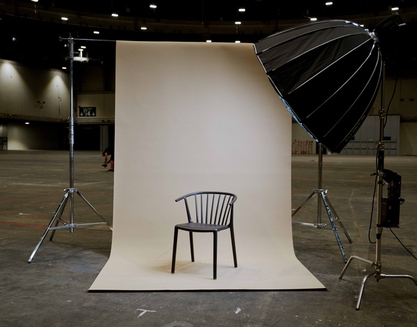 empty black recycled plastic chair in front of beige canvas with big studio lights