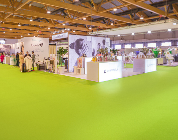 exhibition hall with stands and beauty products, wooden ceiling beams, bright green carpet floor