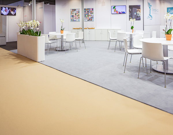 exhibition room with white chairs and tables, light grey event carpet in front of beige sustainable carpet path